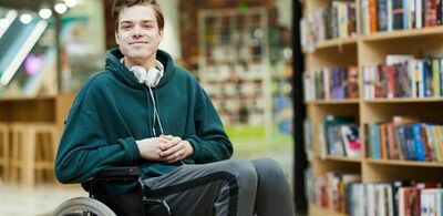 En mann sitter i en rullestol på et bibliotek. Foto
