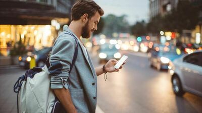 En mann står langs en vei og ser på telefonen sin