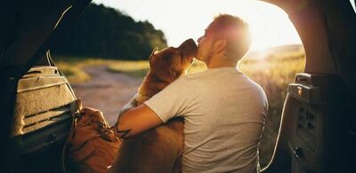 En mann og en hund sitter i bagasjeluken til en bil og koser