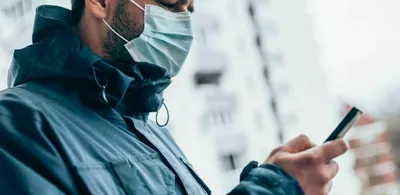 En mann med munnbind ser på telefonen sin