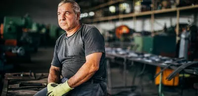 En mann sitter på et bord med arbeidshansker. Foto