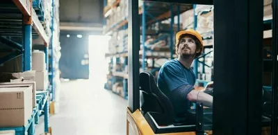 En mann sitter i en gaffeltruck på et lager. Foto