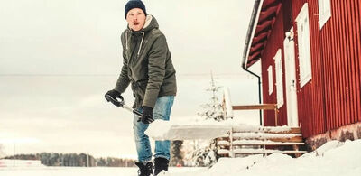 En mann måker snø med en måke. Foto