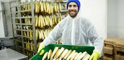 En mann står i hvit kjeledress i et fiskelager, mens han holder en kurv med fisk. Foto