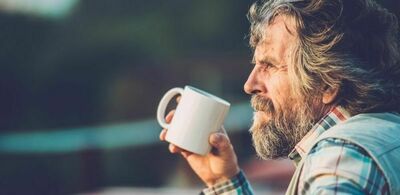 En mann med langt hår og skjegg drikker kaffe utendørs. Foto