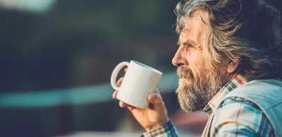 En mann med langt hår og skjegg drikker kaffe utendørs. Foto