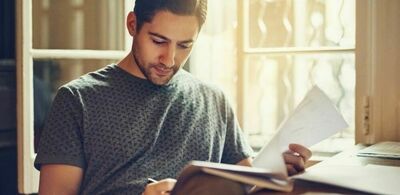 En mann leser og noterer i en bok. Foto