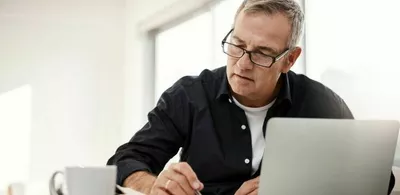 En mann sitter foran en laptop og tar notater. Foto