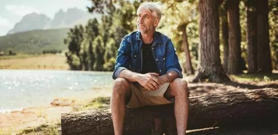 En mann sitter ute i naturen på en trestamme. Foto